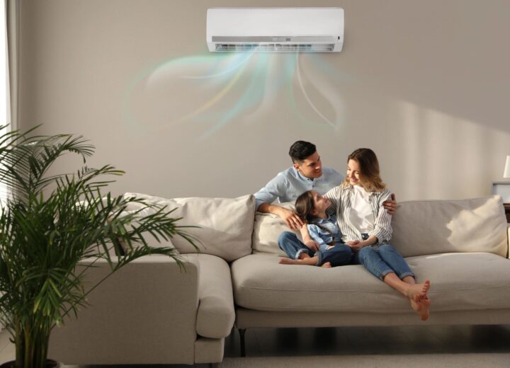 A family relaxes on a sofa under a wall-mounted air conditioning unit.