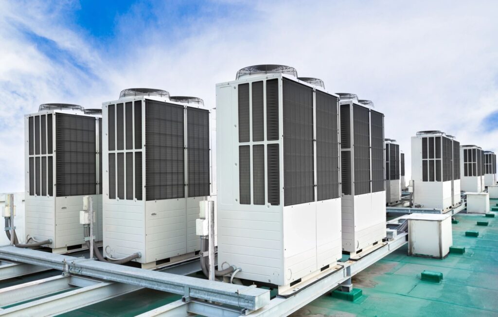 A row of large commercial rooftop HVAC units under a partly cloudy sky.