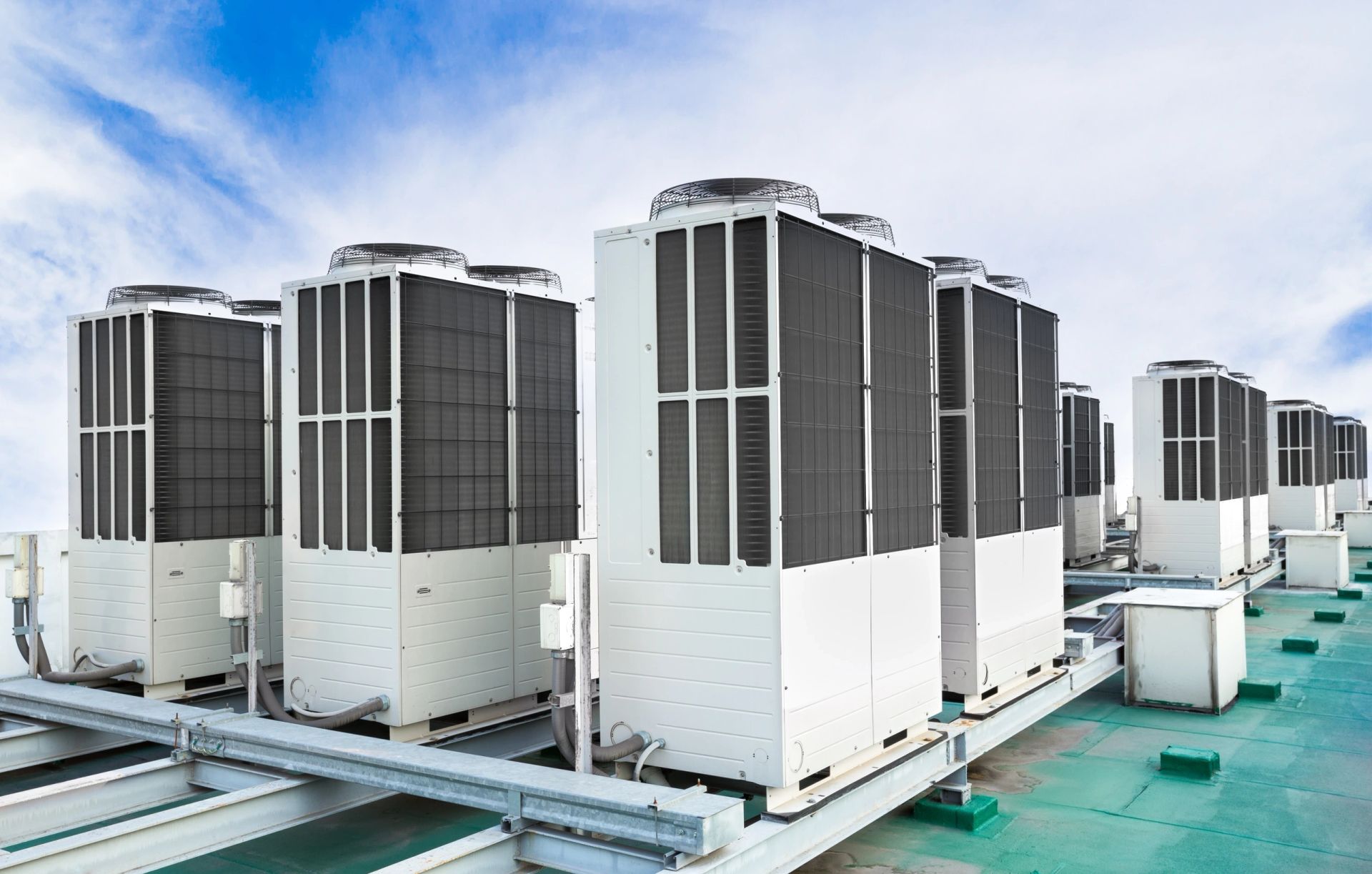A row of large commercial rooftop HVAC units under a partly cloudy sky.