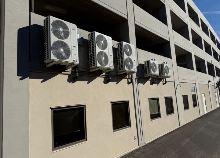Multiple outdoor AC units are mounted on the side of a commercial building.