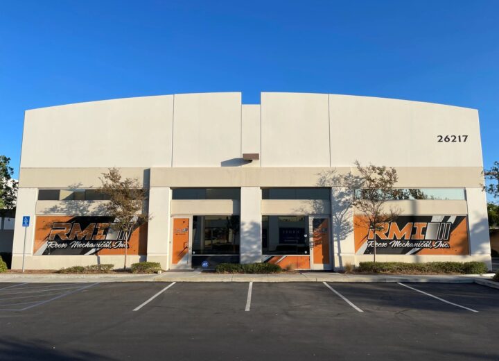 An empty commercial building with a large parking lot under a clear sky.