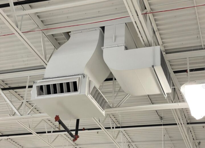 White industrial ductwork and vents are mounted on a ceiling.