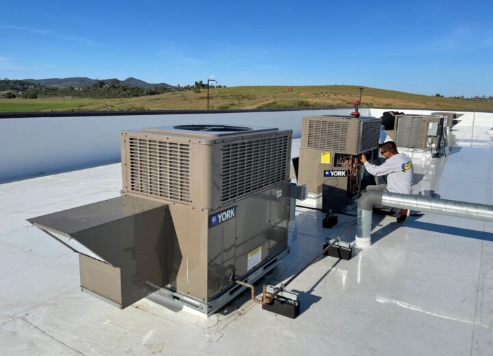 Multiple commercial rooftop HVAC units and ductwork under a clear sky.