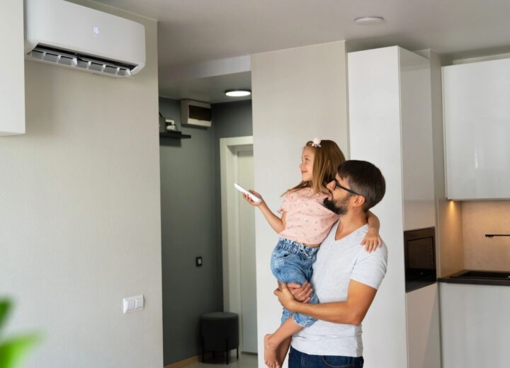 A man holds a child while looking at an indoor air conditioning unit in a modern room.